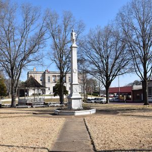 Tall stone monument and gazebo on park with town buildings in the background