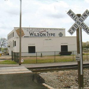 Multistory buildings inside fence with railroad tracks in the foreground