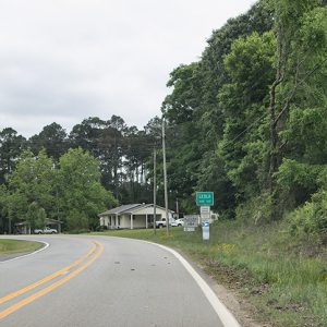 Green "Leola" sign on right side of two-lane road with single-story houses in the background