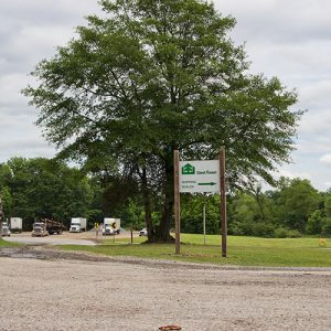 Green and white sign on street corner with semi-trucks parked in the background