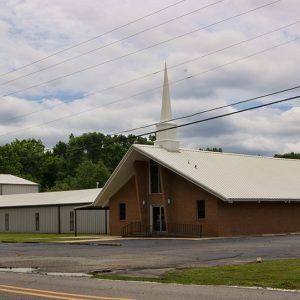 Brick church building with steeple and brick sign on parking lot