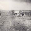 Dirt road with single-story storefronts and car in the background