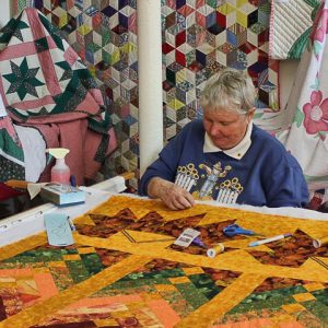 White woman in sweatshirt working on a colorful quilt