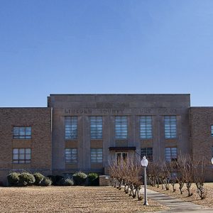 Three-story building with street lamps and bushes lining sidewalk