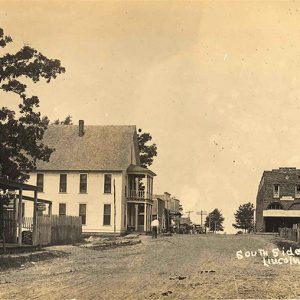 Looking up street with hotel and storefronts on the left and two-story brick building in the background