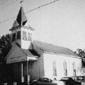 Church building with central bell tower and cars parked alongside