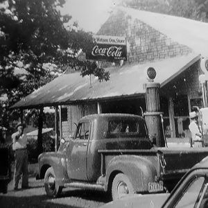 White men and trucks outside single-story storefront with covered porch and Coca-Cola sign