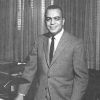 African-American man in suit and tie smiling at his desk