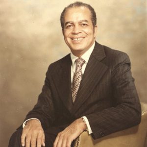 African-American man smiling in striped suit and tie sitting in leather chair