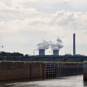 Concrete dam locks and water with three smoke stacks in the background