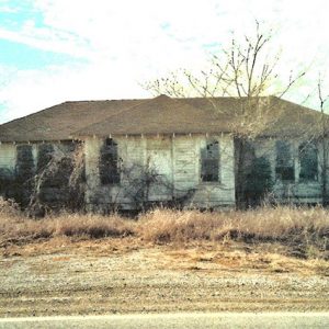 Overgrown and abandoned school house in field