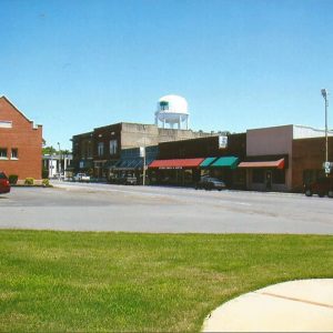 Row of brick storefront buildings on street with water tower in the background