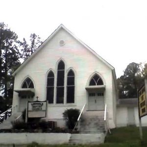 symmetrical white church building with two entrances with stairs leading up to them and sign