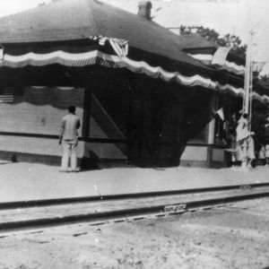 Pair of railroad tracks with depot building and patrons