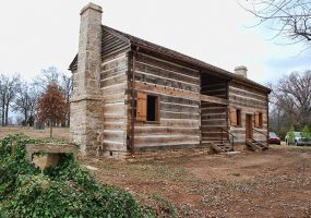 Wood cabin building on dirt with stone chimney