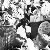 Angry white crowd surrounding young African-American girl sitting on bench with white woman talking to her