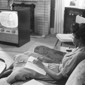 African-American girl taking notes during a television class at home