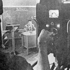 White man speaking at desk with white hand working camera in the foreground