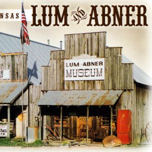 postcard of "Lum and Abner" store and museum fronts with porches signs U.S. flag