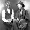 Two white men in costume sitting on a wooden bench