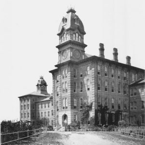 Tall building with arched windows, three chimneys, and a clock tower