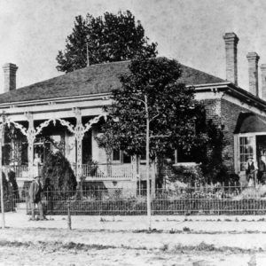 Brick home five chimneys greenhouse with man wrought iron porch with woman pedestrian on sidewalk