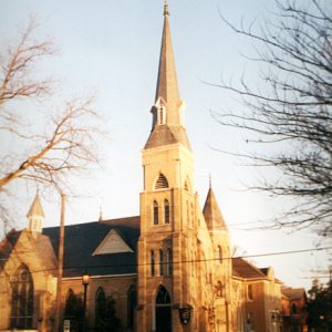 Large brick church with multi story steeple on street corner with bare winter trees