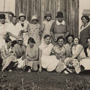 White man in suit and tie sitting with group of white women in dresses outside church building