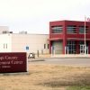 Concrete building with three flags, a bell and a sign "Mississippi County Law Enforcement Center Luxora Arkansas" in front