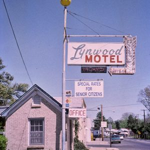 Single-story brick building and hanging "Lynwood Motel" sign on multilane street