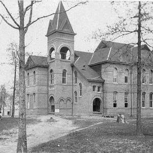 White men and women outside multistory brick building with front tower