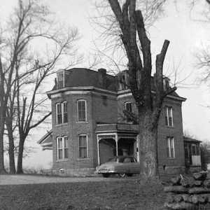 Multistory brick house with car and tree in front yard