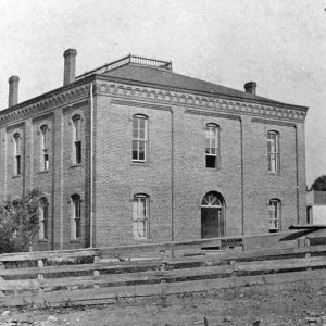 Two-story brick building and outbuilding inside wooden fence