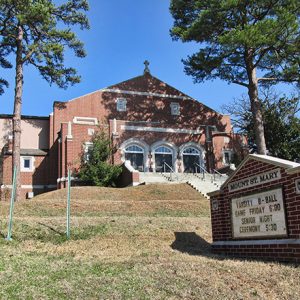 Brick building on hilltop with cross on top stairs and sign