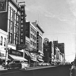 Traffic driving by row of multistory store buildings with neon signs