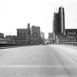 Looking across highway bridge towards oncoming traffic and city buildings in background