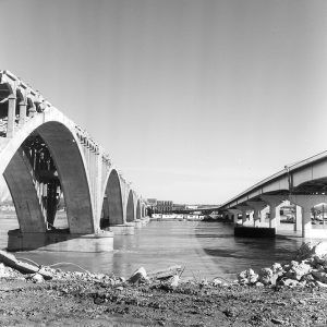 Concrete highway bridge over river next to concrete arch bridge in process of being demolished