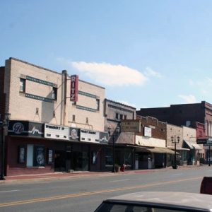 Theater and brick storefronts on street with parked cars on right side