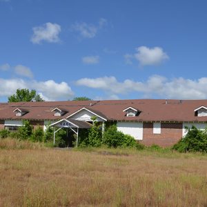 Overgrown abandoned one-story building with covered windows and sagging roof