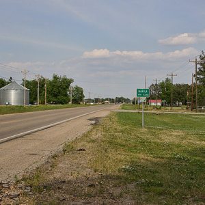 Three silos and power lines on two-lane road across from "Manilla" road sign