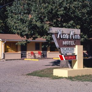 Single-story building behind tree with sign in the foreground