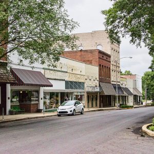 Brick storefronts with trees and parked car on street