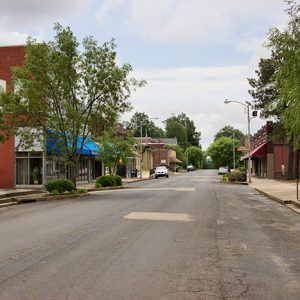 Street with two-story storefronts trees and parked cars