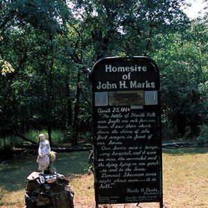 Statue of girl on rock pedestal next to "Homesite of John H. Marks" sign