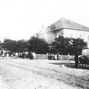 Two-story brick building on dirt road with white residents and storefronts