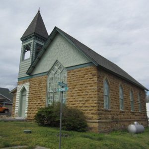 Brick church building with bell tower on street corner with road signs in yard