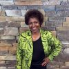 African-American woman smiling in green jacket with stone brick wall behind her