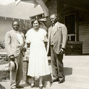 Two African-American men in suits with woman in dress outside house