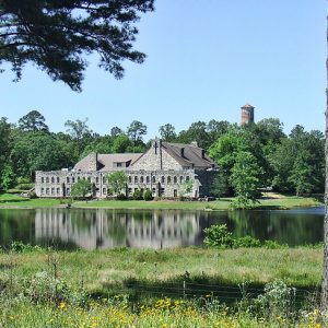 Pond with stone multistory monastery and water tower surrounded by trees