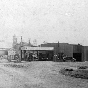 Service station on dirt road with multistory building with clock tower in the background